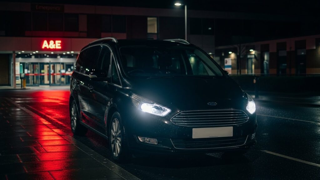 A black private hire taxi waiting outside the University Hospital North Durham Emergency entrance at night, bypassing the locked main doors.